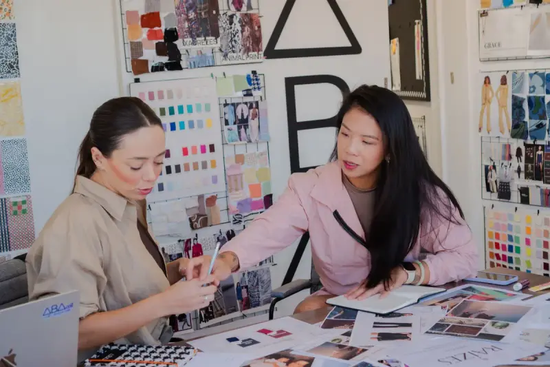 Two women designers reviewing fabric swatches and sketches at a studio table