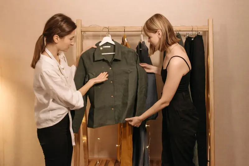 Two women examining a green button-up shirt from a clothing rack in a studio