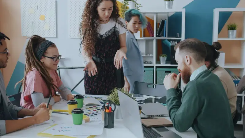 Creative team gathered around a table with laptops and color samples in a bright office