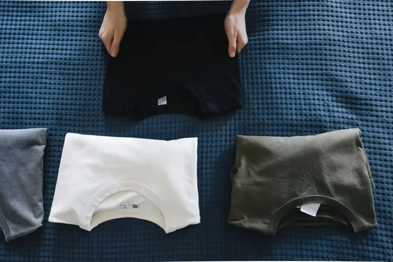 Folded t-shirts in black, white and olive laid out on a blue textured surface