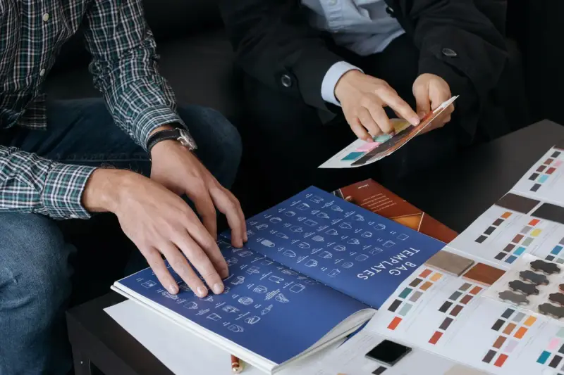 Two people reviewing a sample book and color swatches for bag designs