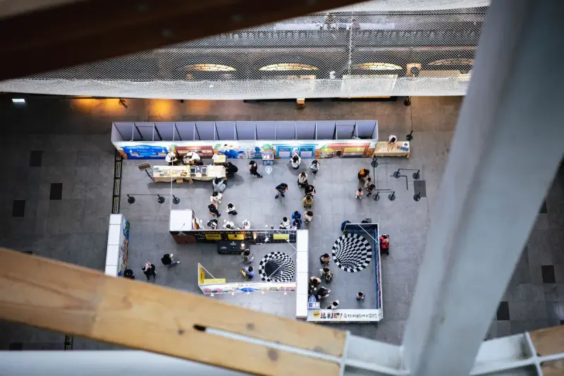Top-down view of an indoor exhibition with stands and visitors moving between them