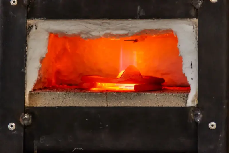 Metal part glowing inside the chamber of a small industrial furnace