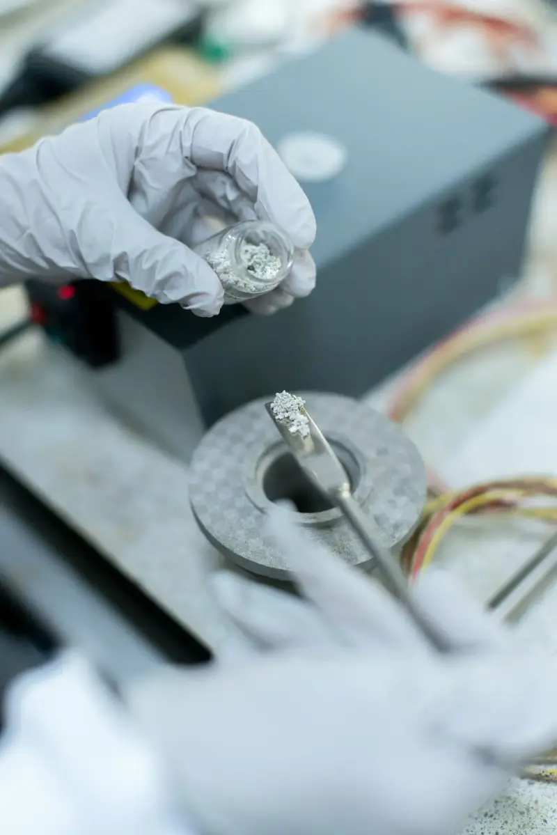 Gloved hands placing a metal sample with tweezers in a laboratory