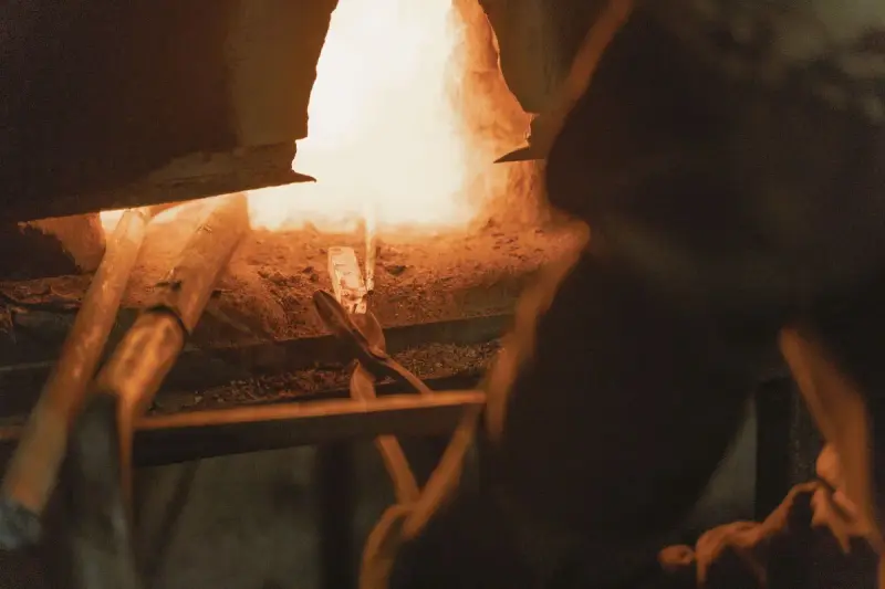 Tongs drawing a steel bar out of a white-hot furnace opening