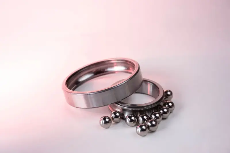 Two polished steel rings beside a cluster of steel balls on a pale pink surface