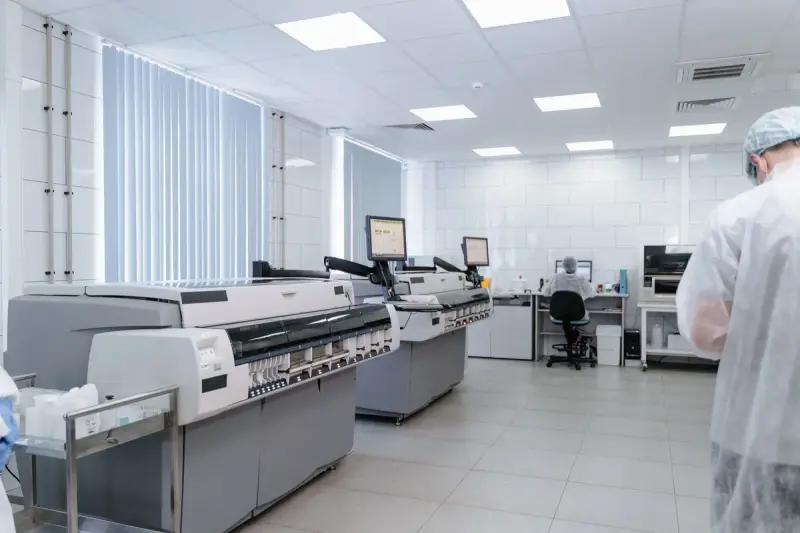 Clinical laboratory with rows of automated analyzers and staff in protective gowns at workstations
