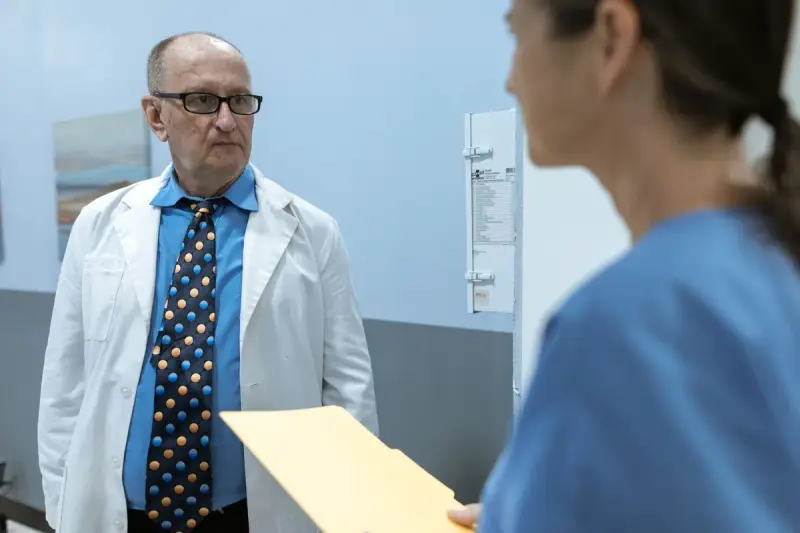 Physician in a white coat talking with a colleague in blue scrubs holding a folder