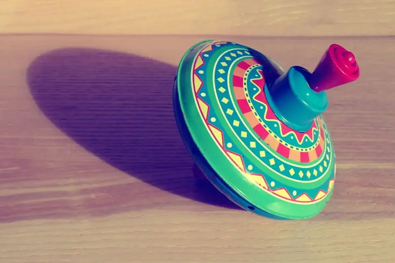Bright patterned tin spinning top casting a long shadow on a wooden table