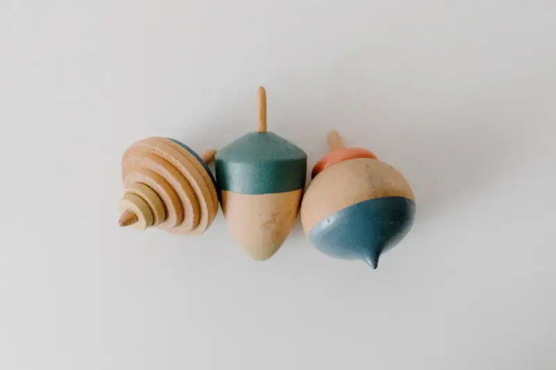 Three small turned wooden spinning tops in natural and teal finishes on a white surface