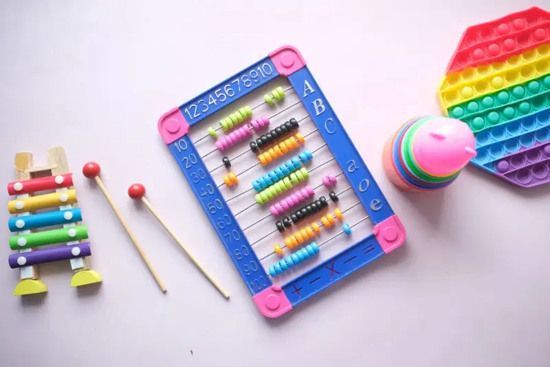 Toy xylophone, bead abacus, stacking rings and a rainbow push-pop toy on a pink background