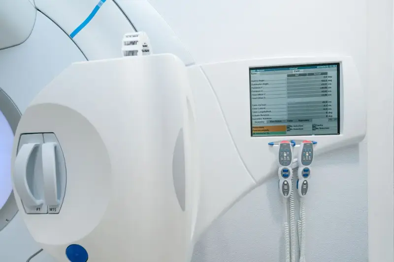 Treatment machine wall screen showing gantry and couch settings, with two hand pendants hanging below