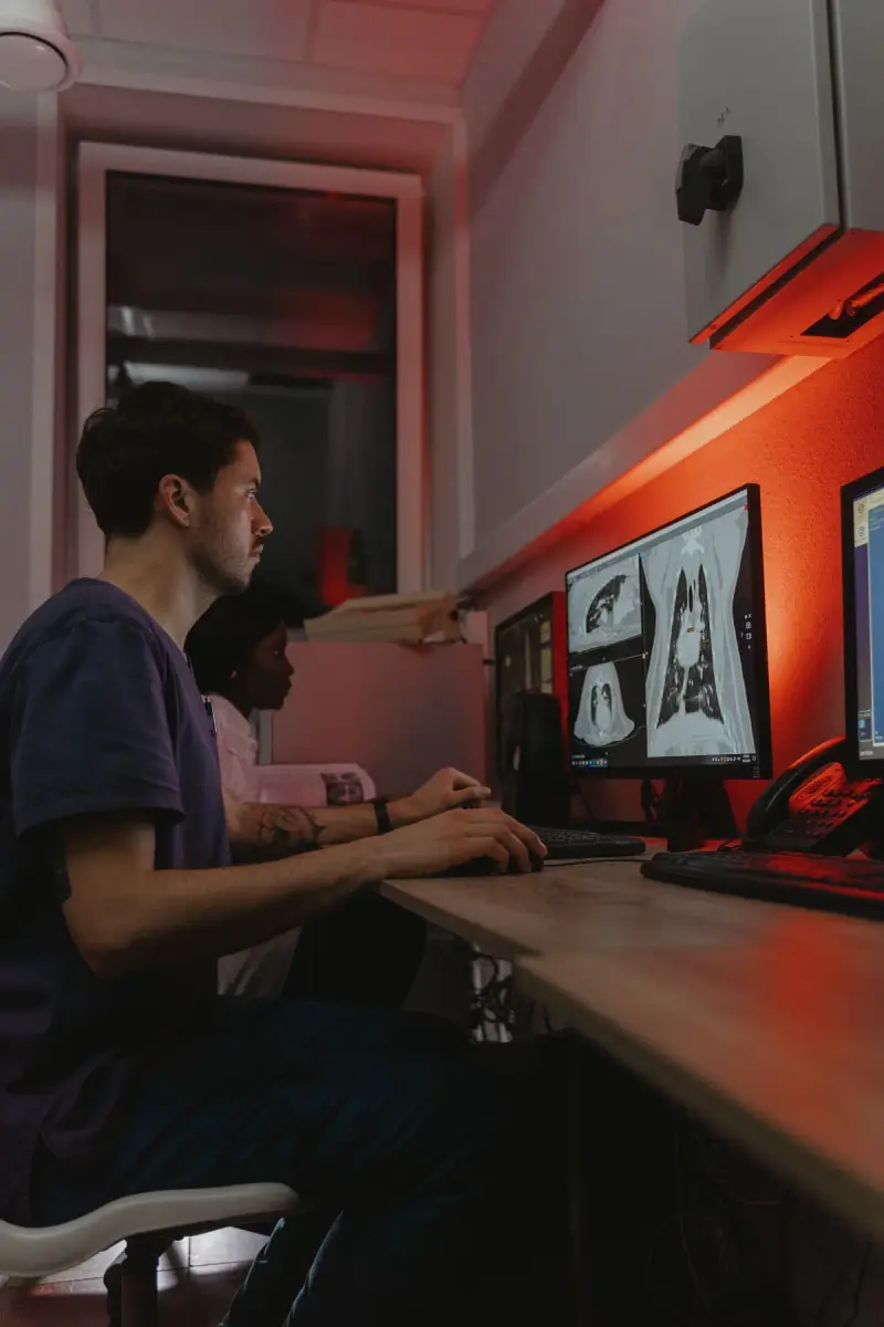 Two clinicians, a man and a woman, studying CT scan images on desktop monitors