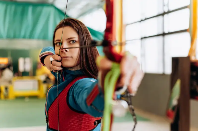Woman drawing a recurve bow at full draw in an indoor range