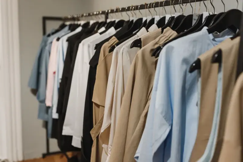 Rack of shirts and trench coats in blue, white and camel on black hangers