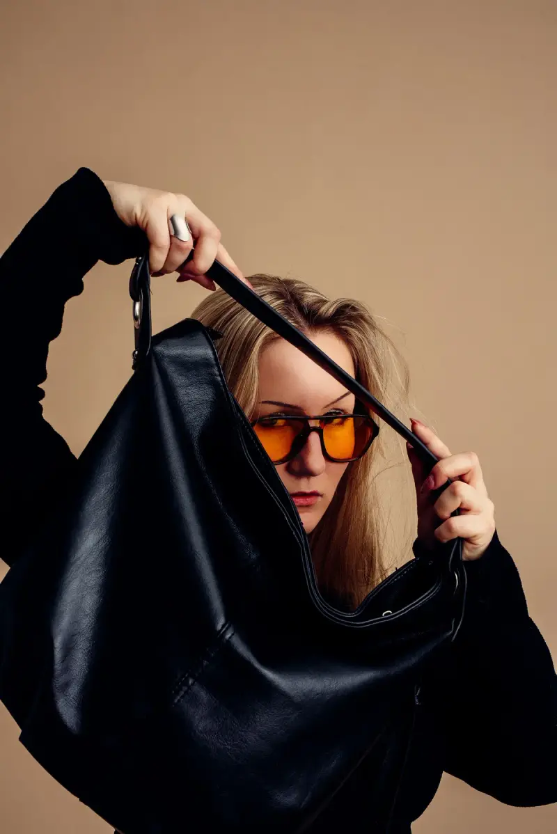 Woman in amber-tinted glasses lifting a slouchy black leather hobo bag