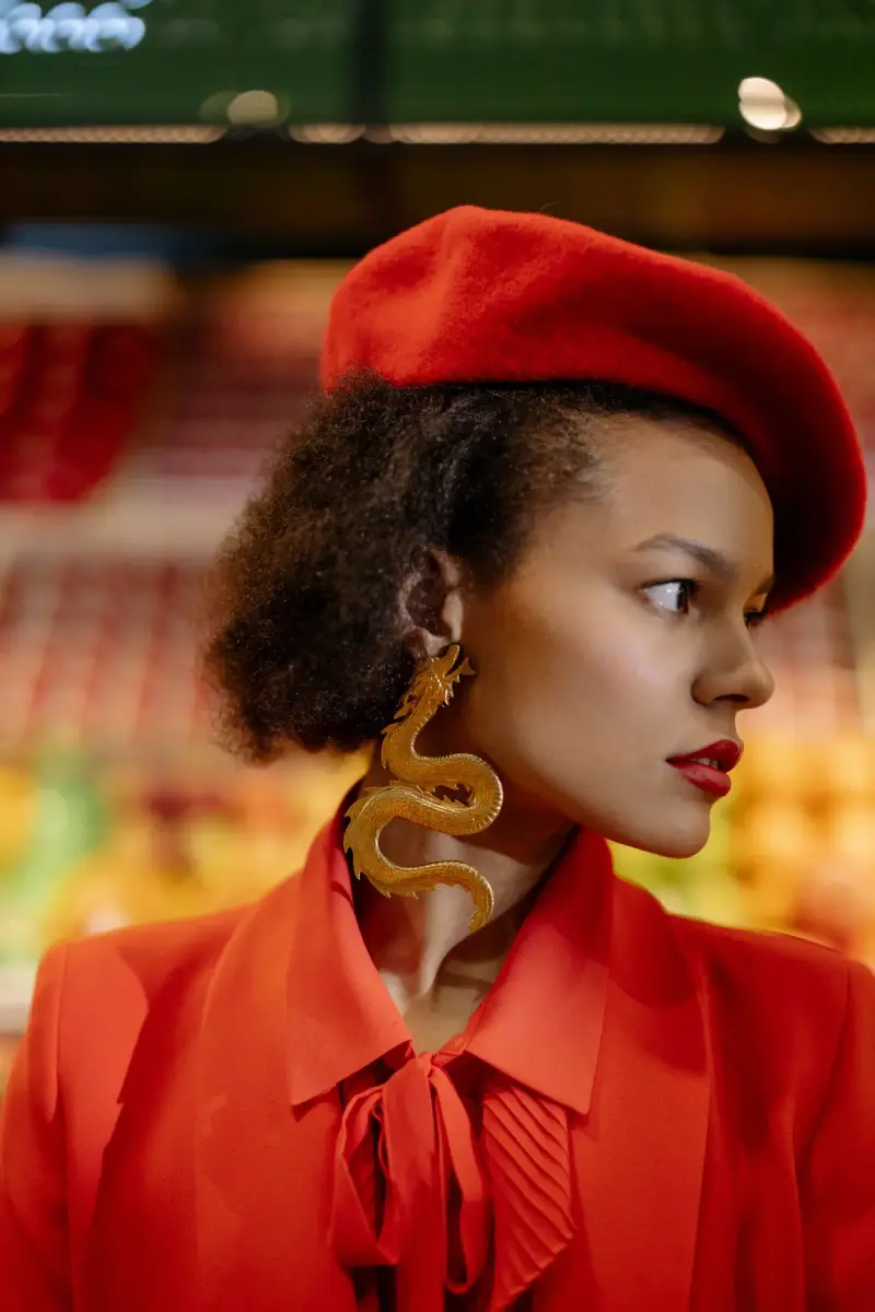 Woman in a red beret, red blouse and a gold serpent earring in profile