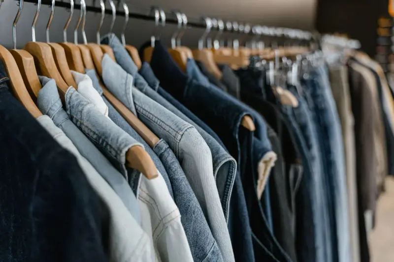 Denim jackets in light to dark washes hanging on wooden hangers