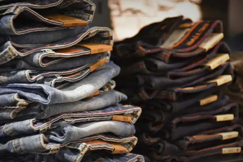 Stacks of folded denim jeans in several washes on a store table