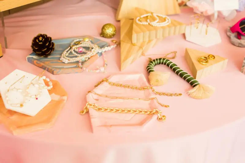 Gold chains, hoops and pearl jewelry displayed on small trays on a pink table