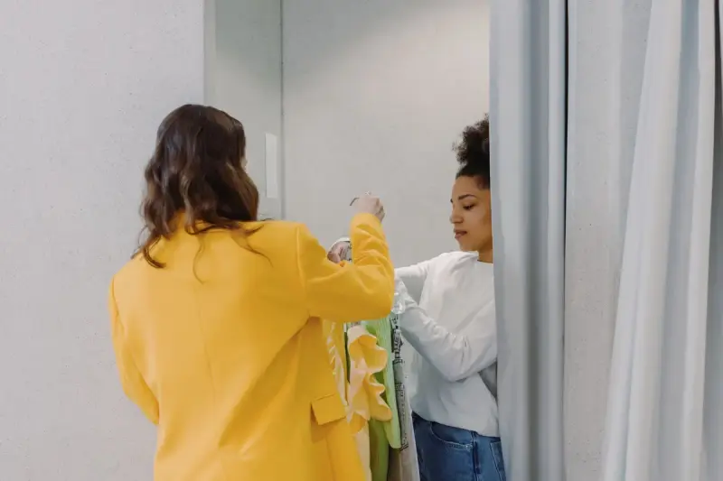 Stylist handing a client garments at a curtained fitting room
