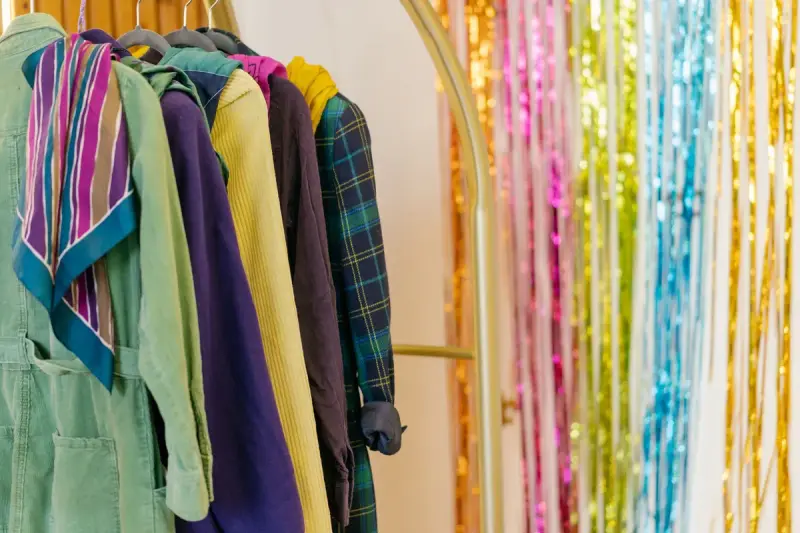 Bright coats, scarves and jackets on a rack beside a colorful tinsel backdrop