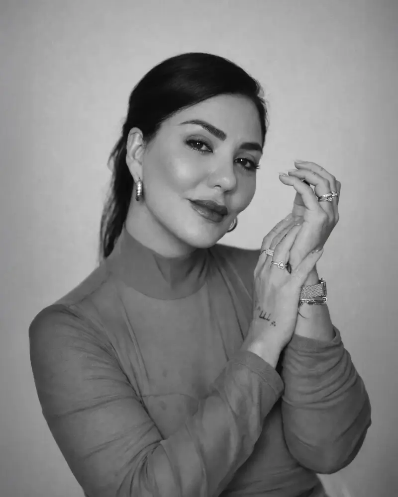 Black and white portrait of a smiling woman wearing hoop earrings, stacked rings and bracelets