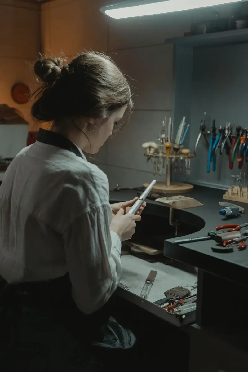 Bench jeweler working at her jewelry workbench with pliers and tools on the wall