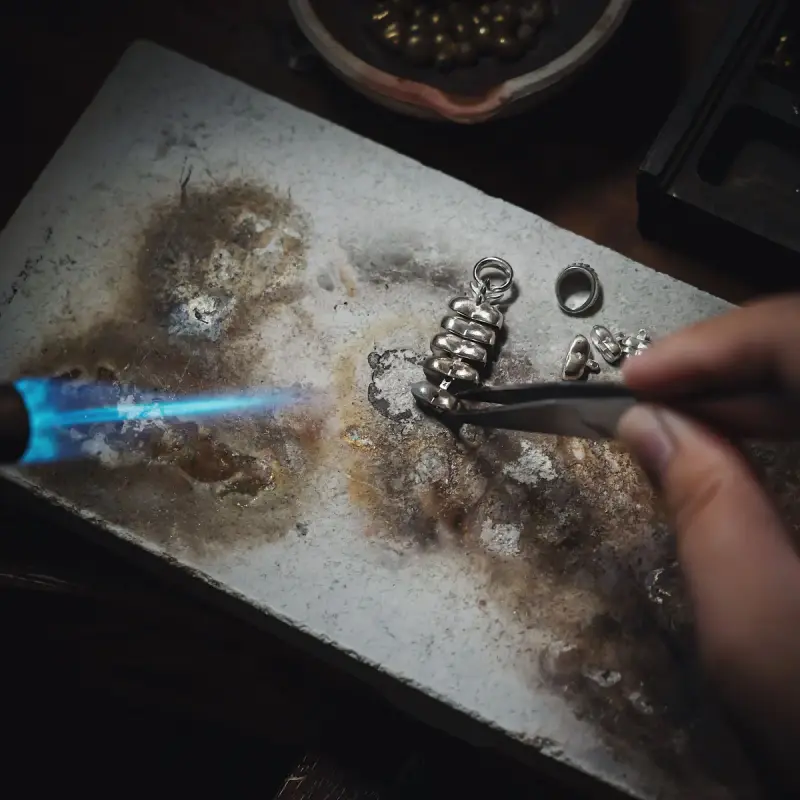 Jeweler soldering a silver piece with a blue torch flame on a soldering block