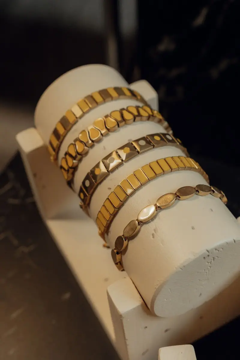 Gold tile and link bracelets stacked on a white bracelet display stand