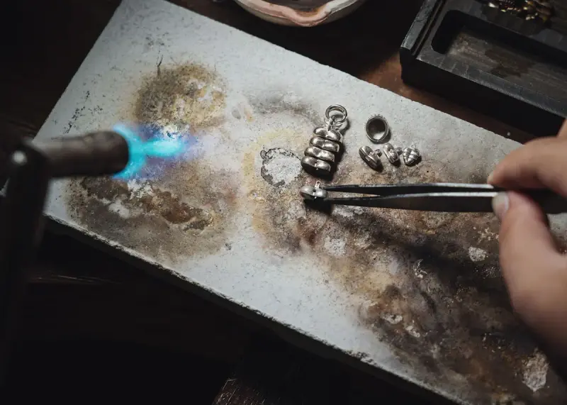 Jeweler using a blowtorch to craft silver pieces on a workbench
