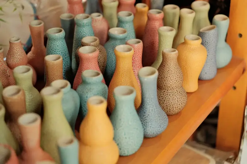 Rows of pastel ceramic bud vases with textured glazes on a wooden shelf