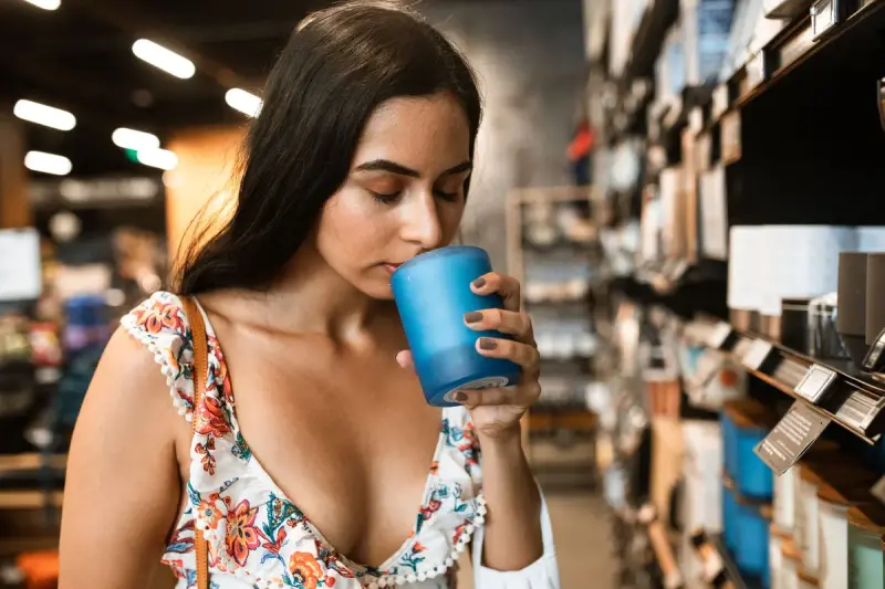 Woman smelling a blue glass scented candle in the aisle of a home goods store