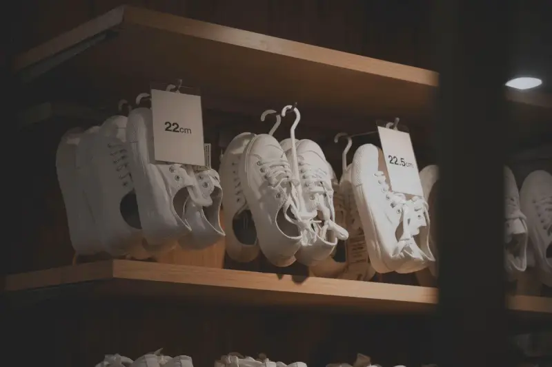 White leather sneakers with size tags lined up on a wooden shop shelf
