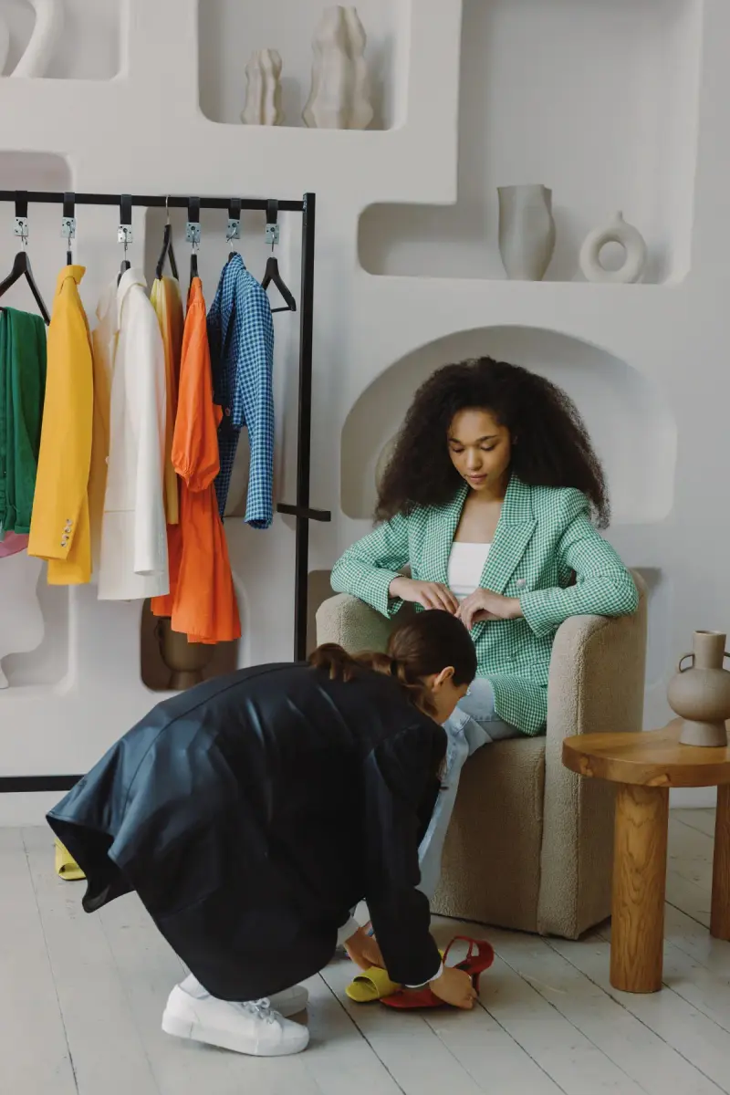 Woman in a mint suit seated in a boutique while a fitter helps her try on shoes