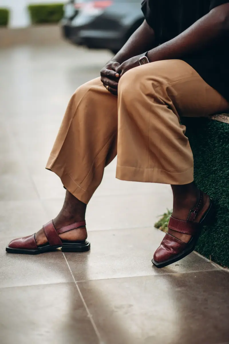 Seated person in camel wide-leg trousers and burgundy leather sandals on a tiled patio
