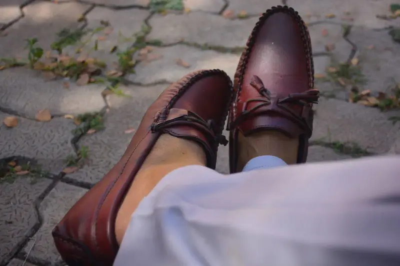 Burgundy leather boat shoes with bow laces worn on a paved courtyard