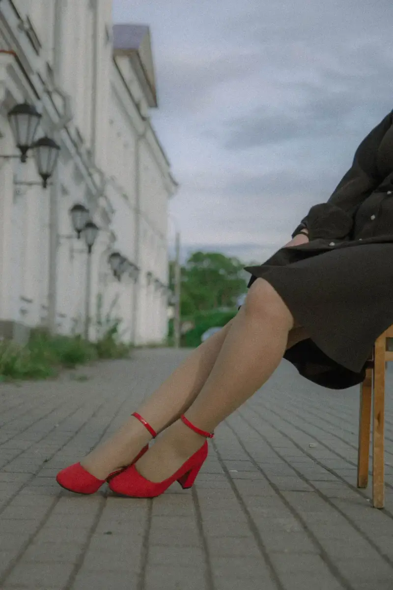 Woman seated on a city sidewalk in red ankle-strap pumps and a dark skirt