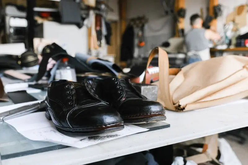 Handmade black leather shoes on a craftsman's workbench among leather offcuts