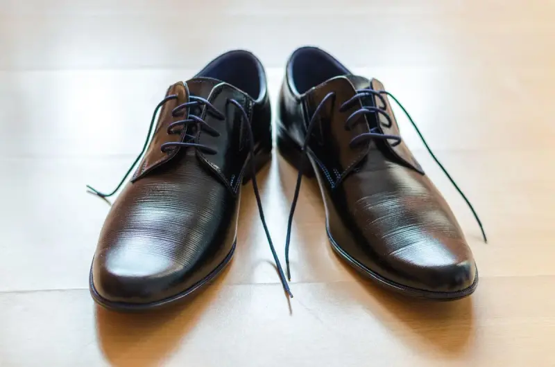 Pair of polished black leather lace-up dress shoes on a light wooden floor