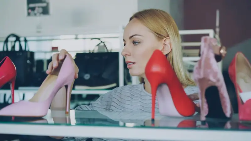 Woman holding a red stiletto while browsing high heels on a store display