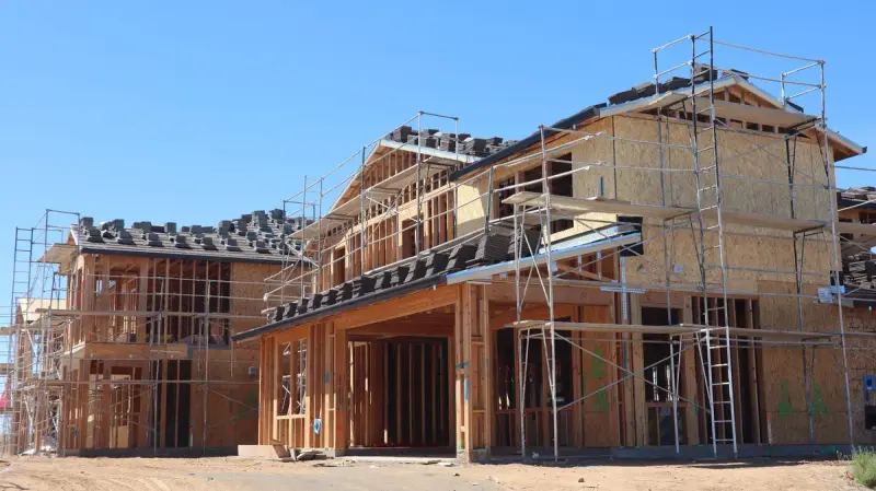 Row of new homes with scaffolding, sheathing and roof tiles staged on the roofs