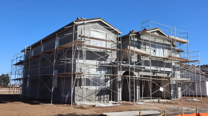 Two-story homes wrapped in scaffolding with grey sheathing on a cleared lot