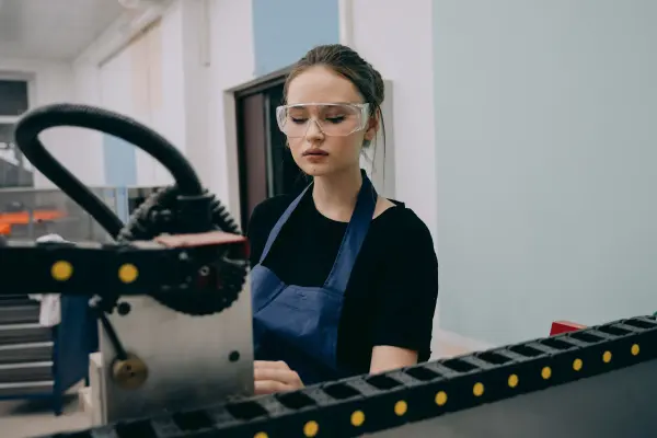 Woman wearing safety glasses working beside industrial machinery