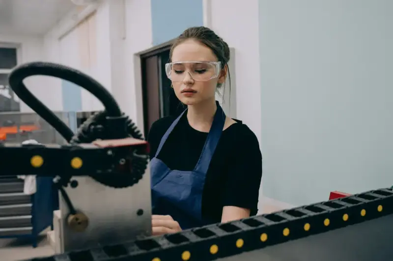 Woman wearing safety glasses working beside industrial machinery