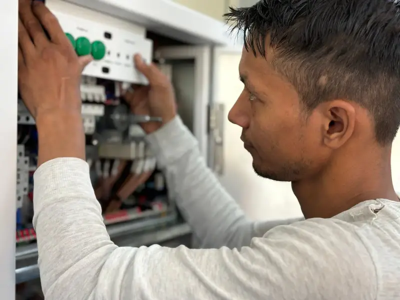 Technician adjusting breakers inside an electrical control cabinet