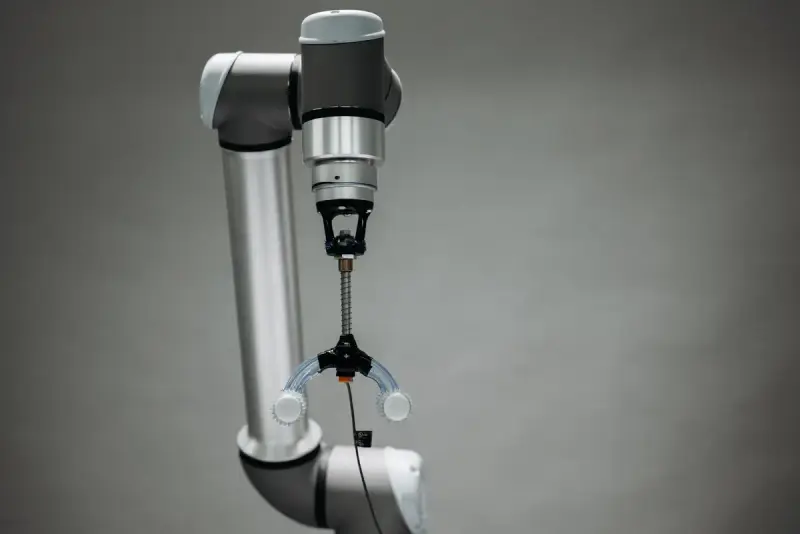 Collaborative robot arm wrist and gripper tool against a plain gray backdrop