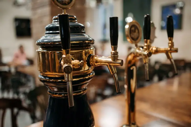 Polished brass draft beer towers with black tap handles on a wooden bar