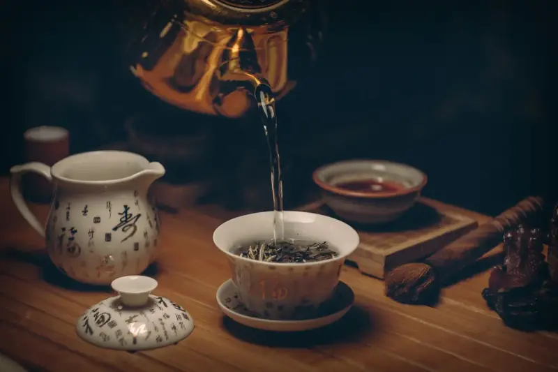 Gold kettle pouring hot water over loose tea leaves in a porcelain cup