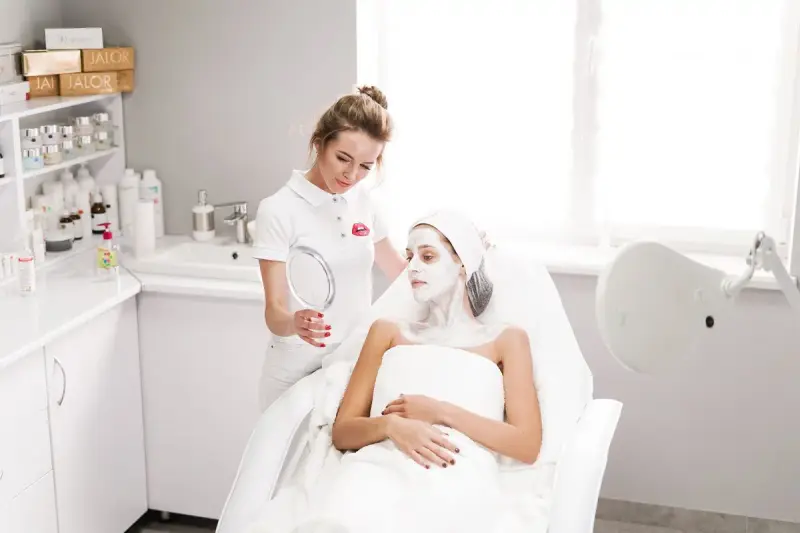 Beautician applying a facial mask to a client in a modern salon